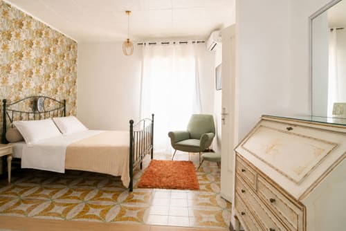 Camera da letto spaziosa presso I colori della Sicilia con carta da parati floreale dorata, letto in ferro nero, poltrona verde e