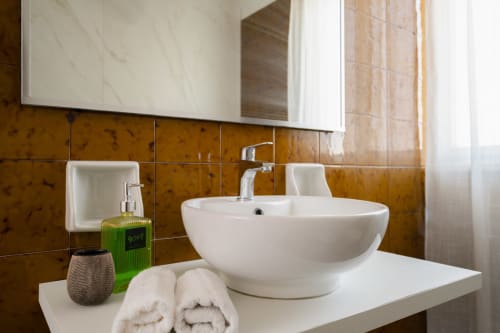 Moderno lavabo bianco con dispenser di sapone verde e asciugamani piegati nel bagno Il Campanile di I colori della Sicilia