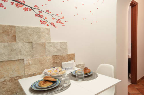 Sicilian apartment dining table set for breakfast with pastries, stone wall backdrop, and red flowering branch decoration