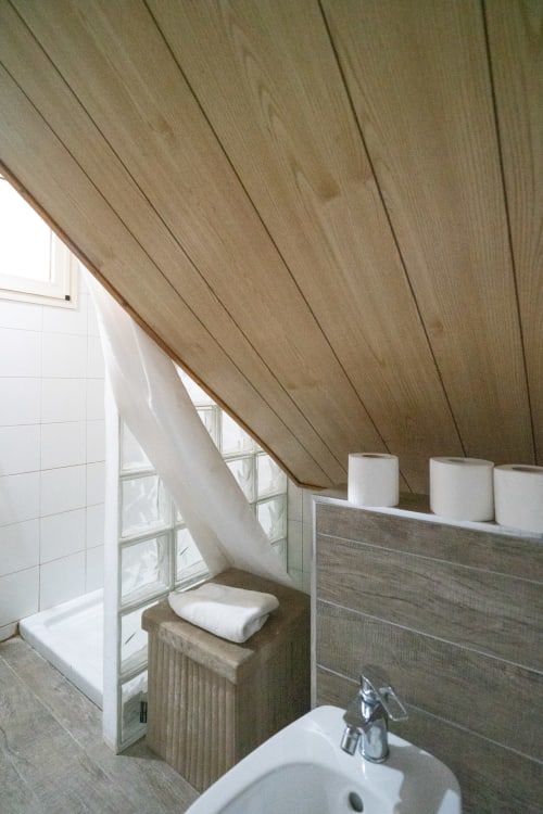 Sloped wood ceiling bathroom with sink, shower enclosure, and window at I colori della Sicilia, Caltagirone