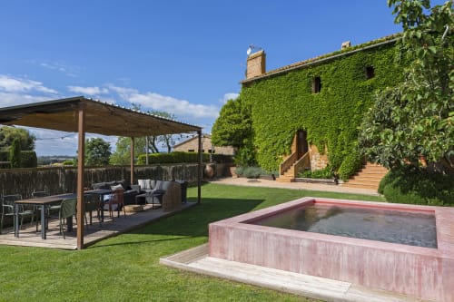 Cour toscane à Apartmentos Rectoria de Regencós avec villa couverte de lierre, piscine et pergola en bois.