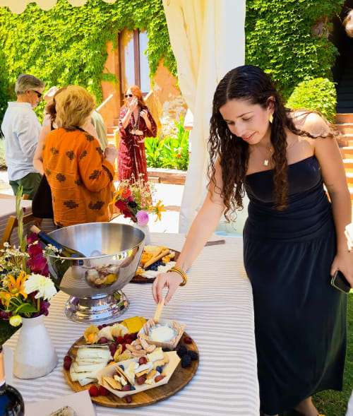 Femme en robe noire à une réception en jardin avec plateau de charcuterie, murs de lierre à l'hôtel Costa Brava