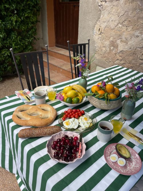 Petit-déjeuner en terrasse à la maison de Costa Brava avec nappe rayée, fruits frais, pains et fleurs dans le jardin