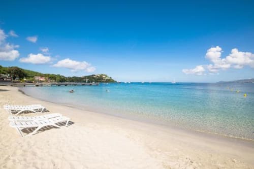 Plage immaculée avec transats blancs, eau turquoise et bâtiments côtiers à l'Hôtel Maison Clémentine à Fort-de-France