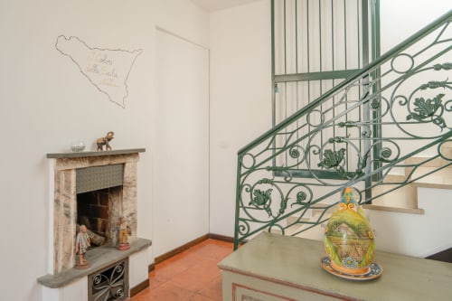 Interno di appartamento siciliano con scalone verde ornamentale, camino, pavimenti in cotto e ceramiche decorative