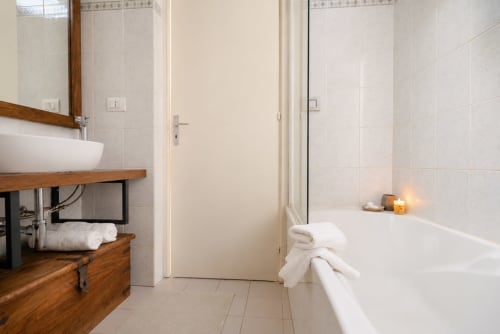 Bagno moderno dell'appartamento La Tegola a Caltagirone con vasca bianca, lavabo in legno e pareti piastrellate
