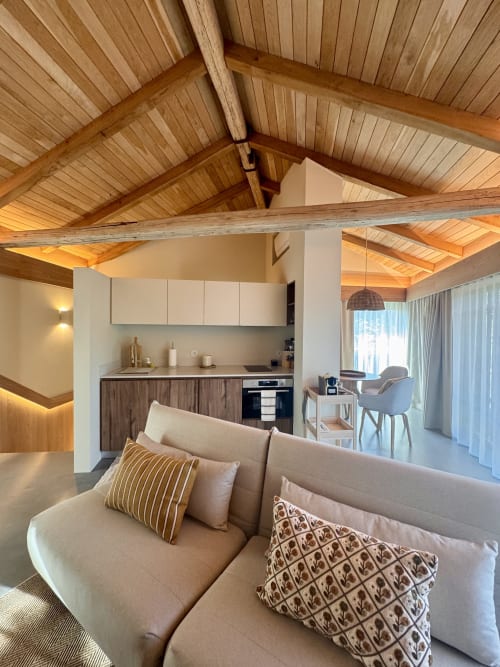 Quinta Das Pirâmides villa bedroom with wooden beam ceiling, cream sofa, and kitchenette in Vila Nova de Famalicão