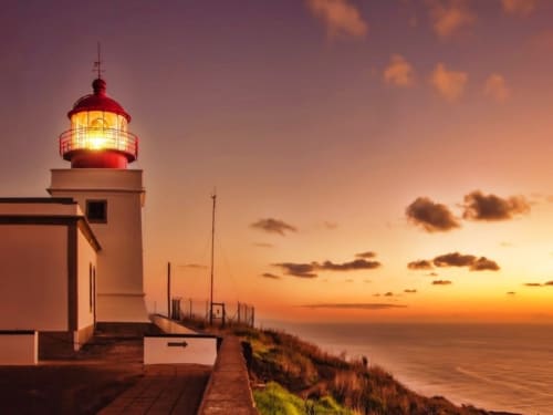 Vista do pôr do sol no farol de Arco da Calheta com céu dourado e horizonte do oceano em Portugal