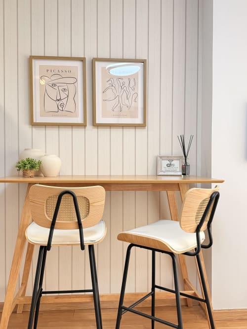 Espacio de trabajo moderno en Sinese Design Homes, Málaga con escritorio de madera, taburetes y obras de Picasso en pared blanca