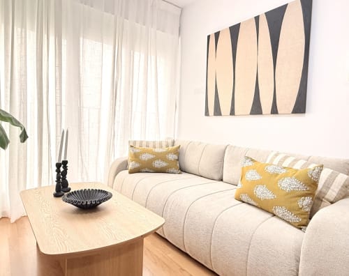 Sala moderna en Sinese Design Homes, Málaga con sofá crema, cojines mostaza, mesa de café de madera y pared abstracta