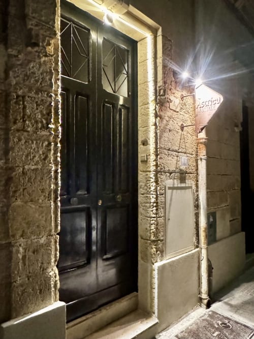 Ingresso in legno nero dell'appartamento HABITARE Àstricu nel centro storico di Lecce, illuminato di notte