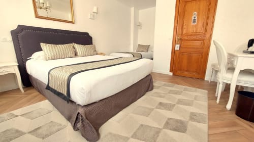 Chambre triple spacieuse à l'Hôtel Dandy Rouen avec lit à tête de lit noire, literie rayée, tapis à motifs et porte en bois