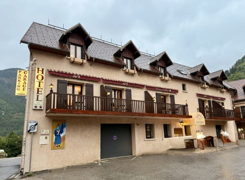Façade de l'Hôtel le Tilleul à Corps, France : murs crème, toit mansardé foncé, balcons bois, panneau de parking