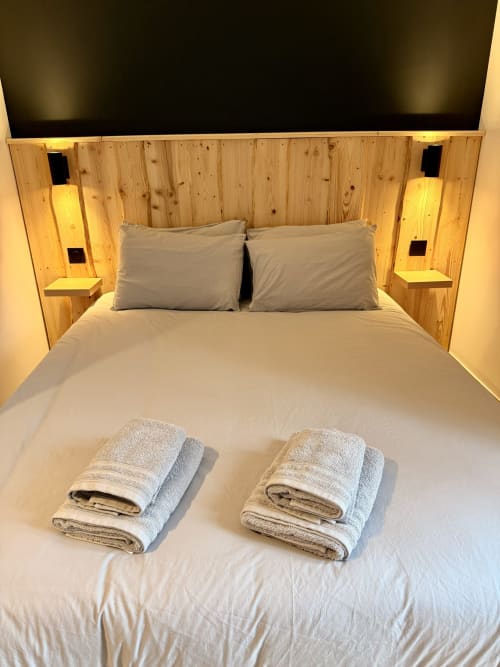 Lit double moderne avec tête de lit en bois, oreillers gris et serviettes roulées à l'Hôtel le tilleul à Corps