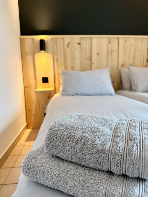 Lit deux places avec serviettes grises à l'Hôtel le tilleul à Corps, France, avec tête de lit en bois et lampe de chevet