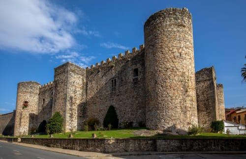 Castillo medieval de piedra en Arenas de San Pedro con torre cilíndrica y muros almenados bajo cielo azul