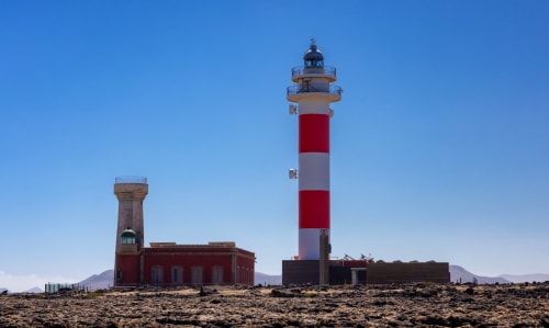 Faro de rayas rojas y blancas cerca de El Cotillo, Fuerteventura con paisaje volcánico y cielo azul