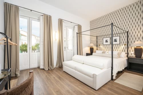 Lujosa habitación de hotel en Málaga con cama con dosel, ropa de cama blanca, papel tapiz decorativo y acceso a balcón en Sinese Design Homes