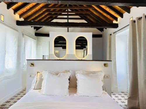 Dormitorio moderno en Sinese Design Homes Málaga con vigas de madera vista, espejos ovalados dorados y ropa de cama blanca