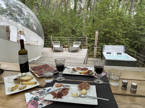 Extérieur du glamping bulle avec plateau de charcuterie raffinée, vin et bain à remous face à la forêt aux Bulles De