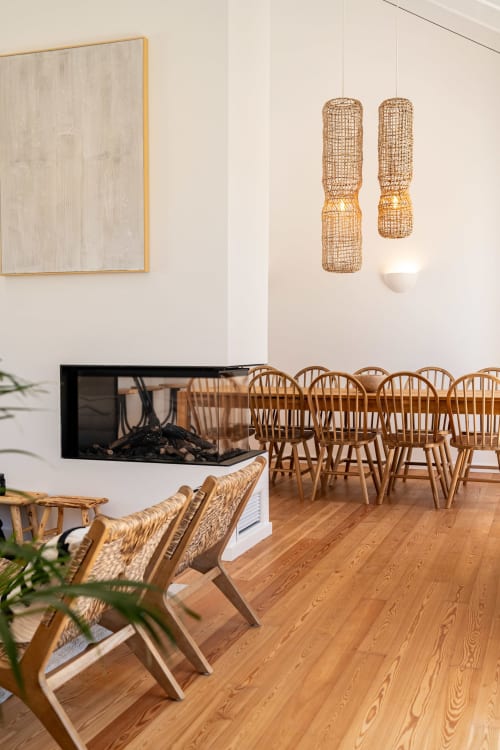 Modern dining area in Sea'Ya Villa Juso with wooden chairs, woven pendant lights, fireplace, and hardwood flooring.