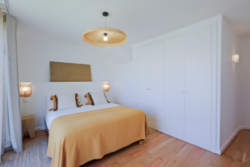 Modern bedroom at Sea'Ya Villa Juso with yellow bedding, woven ceiling light, white wardrobes, and wooden flooring in