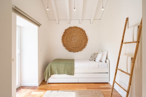 Minimalist bedroom in Sea'Ya Villa with white bed, green throw, circular woven wall art, wooden ladder shelf, and natural