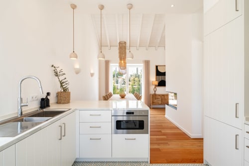 Modern white kitchen with wooden floors, pendant lights, stainless steel appliances, and open dining area with mountain views