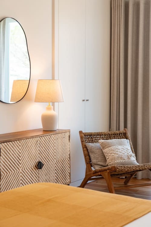 Modern bedroom at Sea'Ya Villa Juso with patterned dresser, pendant lamp, round mirror, and woven chair