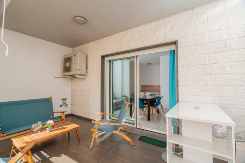 Modern terrace lounge at Short Let's Olbia with teal seating, wooden chairs, and sliding glass doors to dining area