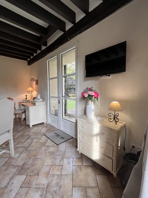 Chambre moderne au Colombier de Hanches avec télévision écran plat, commode blanche avec fleurs roses et portes donnant sur le jardin