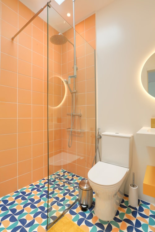 Baño moderno en El Patrón Casa de Huéspedes con ducha de azulejos naranjas, piso geométrico colorido y espejo iluminado