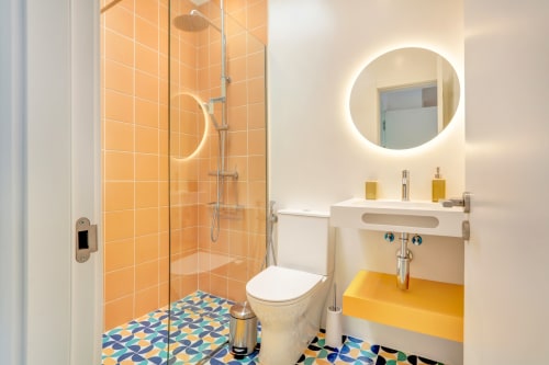 Baño moderno en El Patrón Casa de Huéspedes en El Cotillo con azulejos naranjas, espejo iluminado, tocador amarillo y