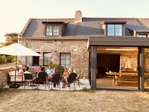 Cottage en pierre du Gîte du Cap Fréhel avec clients réunis sur la terrasse sous parasol et extension moderne à intérieur bois