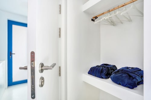 Armario moderno con puerta azul, estantes blancos con ropa azul marino doblada y varilla de bambú en El Patrón Casa de Huéspedes