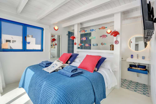 Dormitorio luminoso en El Patrón Casa de Huéspedes, El Cotillo, con cama azul, almohadas rojas, arte marino y decoración náutica
