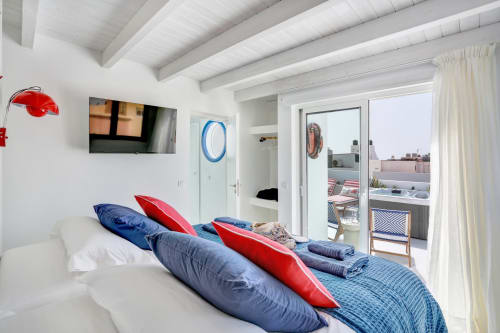Luminosa habitación en El Patrón Casa de Huéspedes, El Cotillo, con almohadas azules y rojas, vigas blancas, TV y acceso a terraza