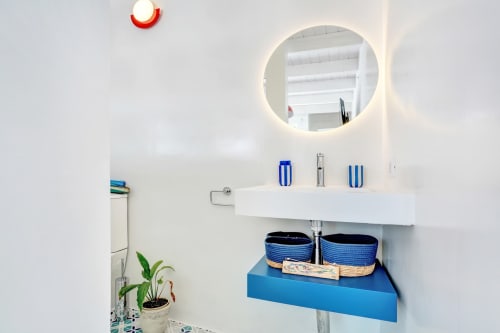 Moderno cuarto de baño en Habitación Faro de El Patrón Casa de Huéspedes, El Cotillo, con espejo circular y cestas azules de almacenamiento
