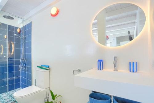 Baño moderno en El Patrón Casa de Huéspedes en El Cotillo con ducha de azulejos azules, espejo redondo y tocador blanco