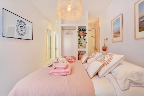 Dormitorio luminoso en El Patrón Casa de Huéspedes, El Cotillo, con ropa de cama rosa, detalles de madera y lámpara de techo tejida