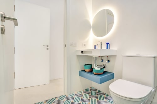 Baño moderno en El Patrón Casa de Huéspedes en El Cotillo con espejo iluminado, lavamanos azul y piso con patrón geométrico