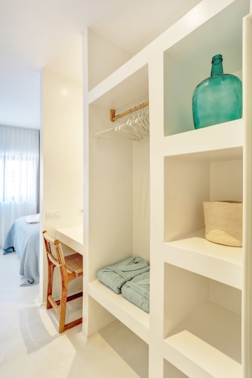 Habitación luminosa en El Patrón Casa de Huéspedes en El Cotillo con estantes blancos empotrados, botella turquesa, silla de madera y