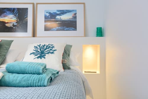 Dormitorio con tema costero en El Patrón Casa de Huéspedes, con acentos turquesas, fotos de atardeceres enmarcadas y iluminación cálida