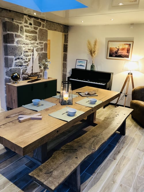 Élégante salle à manger du Gîte du Cap Fréhel avec table en bois, piano, cheminée en pierre et plafond avec lanterneau à Plévenon.