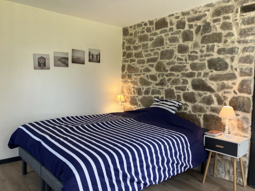 Chambre accueillante du Gîte du Cap Fréhel aux murs de pierre, literie rayée bleu marine et éclairage chaleureux à Plévenon