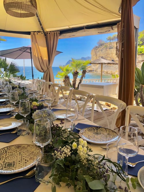 Terraza de comedor frente al mar en Casa Marina Suites, Benissa con vistas al mar, mesas decoradas y palmeras.