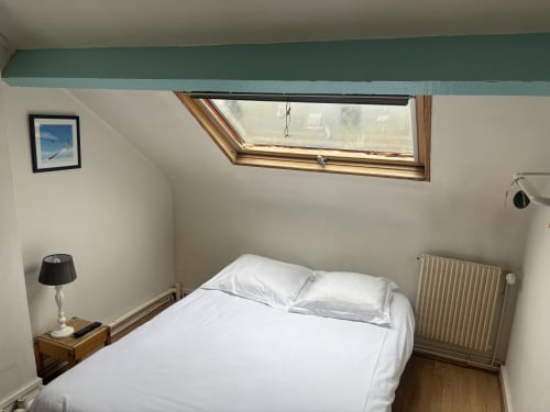 Chambre cosy de l'Hôtel bistrot de la poste avec fenêtre de toit, literie blanche, mobilier en bois et radiateur