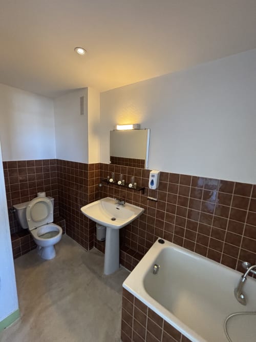 Salle de bains aux murs carrelés marron, lavabo sur colonne, toilettes et baignoire à l'Hôtel bistrot de la poste à Saint-Valery-en-Caux