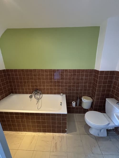 Salle de bain de la Chambre Triple à l'Hôtel bistrot de la poste : carrelage mural brun, baignoire blanche, toilettes et sol en carrelage beige.