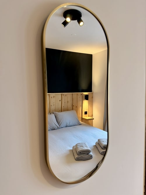 Miroir ovale reflétant la chambre avec tête de lit en bois, literie blanche et serviettes pliées à l'Hôtel le Tilleul, Corps